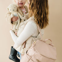 Mom holding toddler. mom is wearing Blush capri backpack