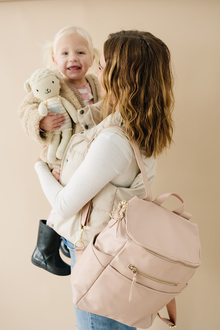 Mom holding toddler. mom is wearing Blush capri backpack