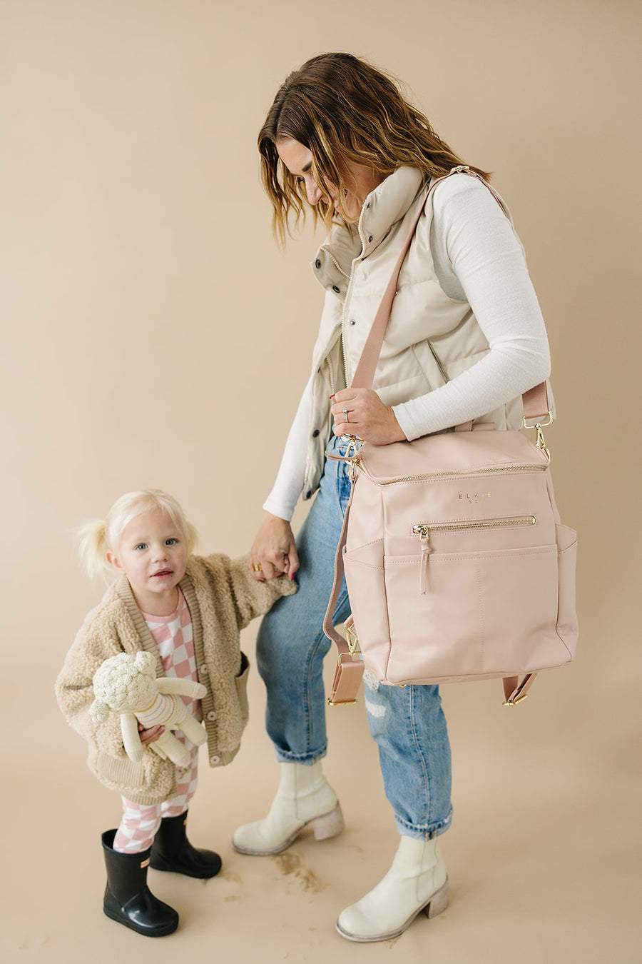 Mom holding toddler daughter hand. Mom is wearing the Blush capri backpack as a shoulder bag