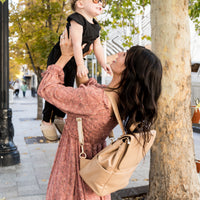 mom throwing up daughter in the air. mom is wearing elkie co milan diaper bag