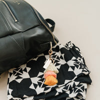 black backpack laying on top of black and white blanket with cream, yellow, and Sherbet pink tiered tassel bag charm.