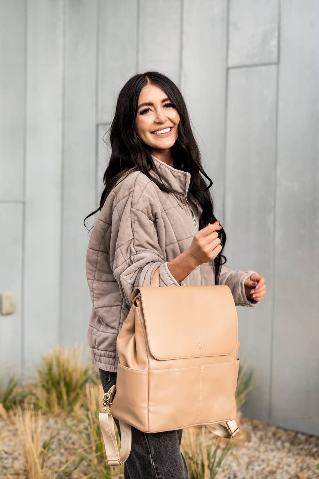 Woman smiling while holding the Tan Milan diaper back by grab handle