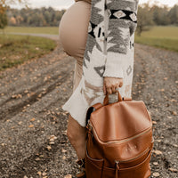 Pregnant woman holding Saddle Capri diaper bag by grab handle