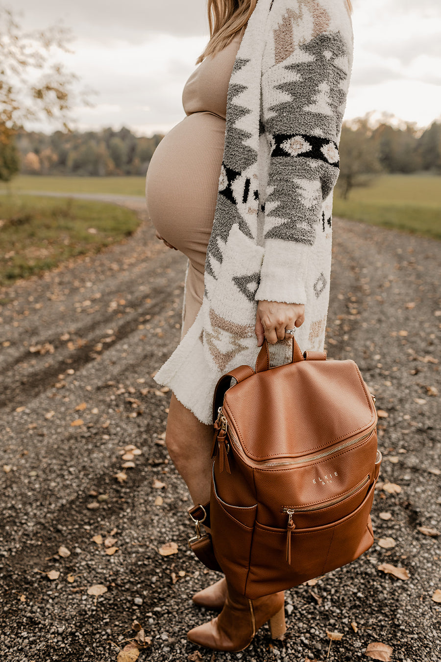 Pregnant woman holding Saddle Capri diaper bag by grab handle