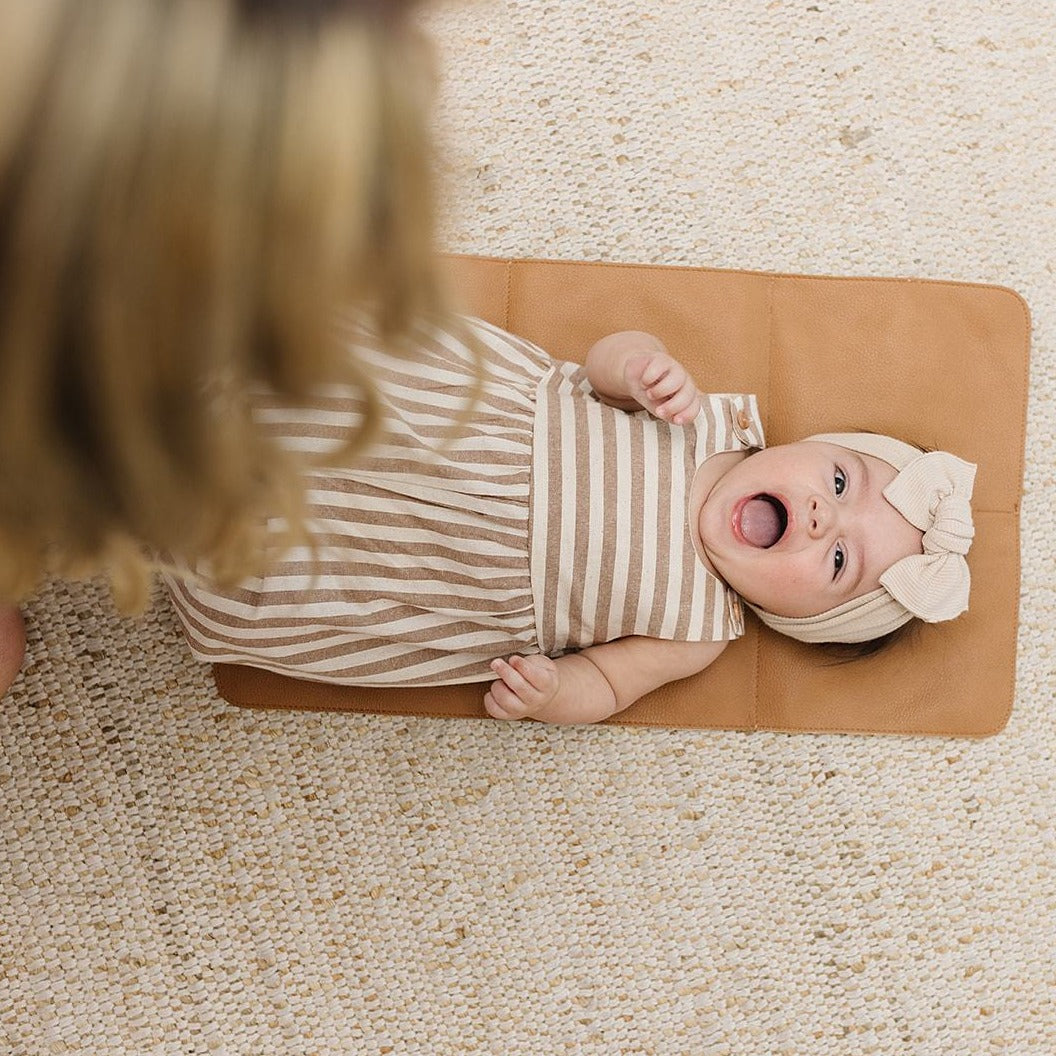 3 month old girl baby with tan and white stripe romper and cream headband with bow on elkie changing mat 