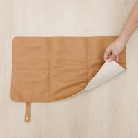 Elkie co Camel cognac tan brown color changing mat on light wood background with asomeone turning over the corner to show the cream color on the reverse side. 