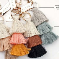 inforgraphic of four tassle bag charms with gold plates that say elkie. Mocha Sherbet Sand Fawn Cedar The Blues