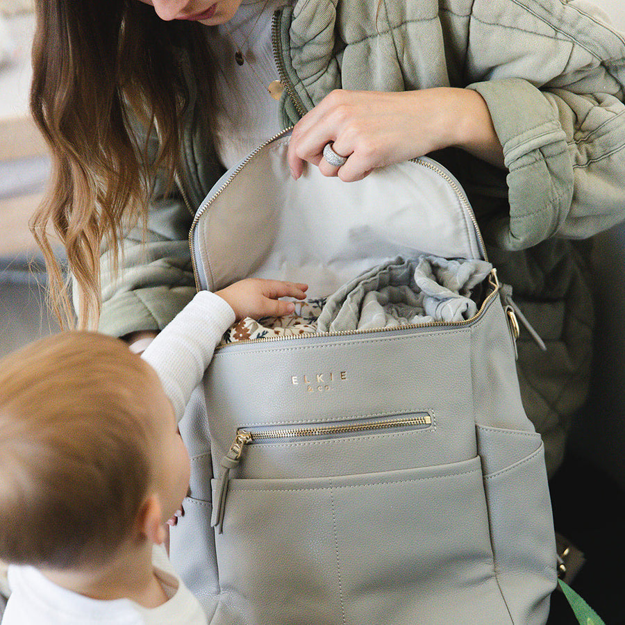 mom opening top of Stone capri backpack with babys hand reaching inside the bag