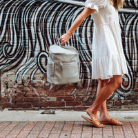 Stone Capri backpack being held by grab handle by woman in white dress and brown sandals
