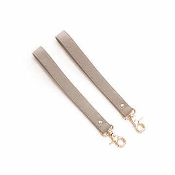 product image with white background showing two taupe color stroller straps laying diagonally next to each other