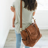 image of backside of woman wear elkie aberdeen diaper bag as a crossbodt. Bag is hanging at her right hip. Ebony Saddle Taupe Tan Stone